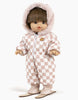 A Minikane Gordis doll with short brown hair wears the Gigi Pink and White Checkered Ski Suit, complete with a fur-lined hood, matching pants, and boots. The set fits perfectly on toddlers 34 & 37cm. The doll stands upright with arms slightly outstretched, accessorized with the charming “Mitten” Pin.