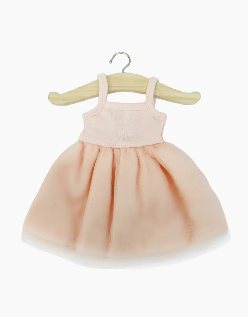 A charming Minikane Doll Clothing piece, the Rosella Tutu in Pale Pink, is displayed on a wooden hanger against a plain white background. This light pink sleeveless dress features a fitted bodice and a flared skirt, designed in France for an elegant touch. It's hand washable for easy care.