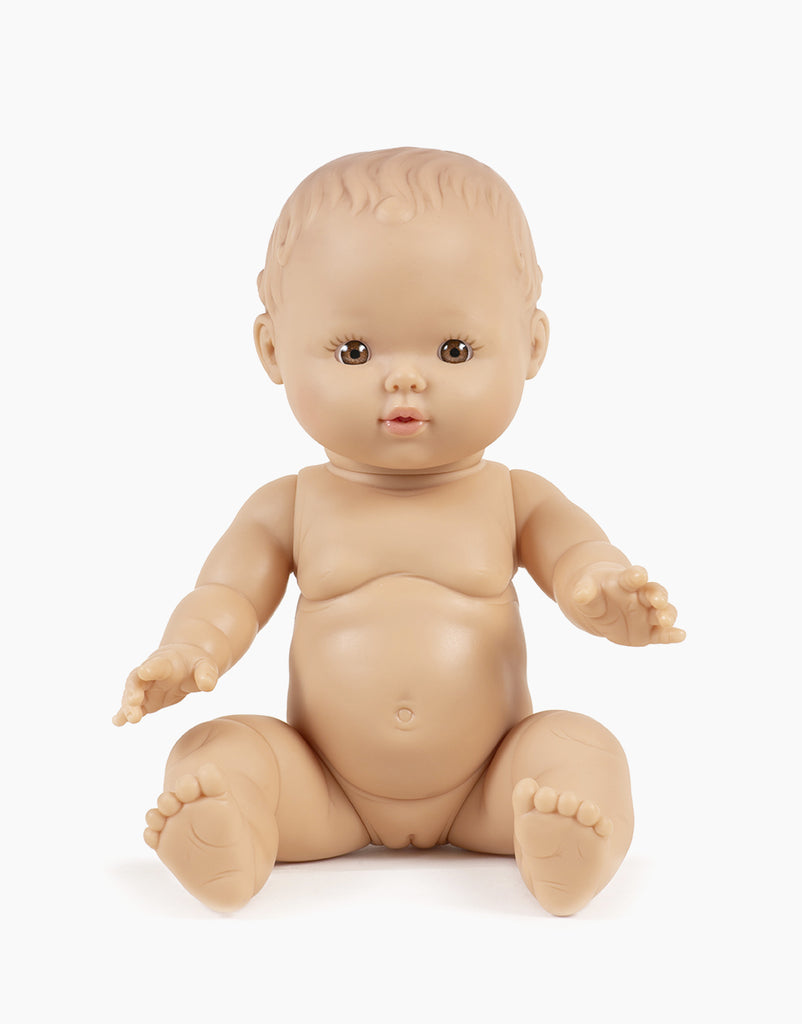 A close-up of a 13-inch Minikane Doll named Faustine, seated upright against a plain white background. The nude baby doll, made from phthalate-free vinyl, displays short painted hair and a neutral expression. Its arms and legs are slightly bent, making it ideal for imaginative playtime. Clothing sold separately.