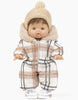 A Minikane Gordis doll with short brown hair is dressed in a plaid-patterned jumpsuit featuring a fur-lined hood. It wears a beige knit hat with a pom-pom and Minikane Doll Shoes in Converse Style White Sneakers, giving it an adorable baby-like appearance.