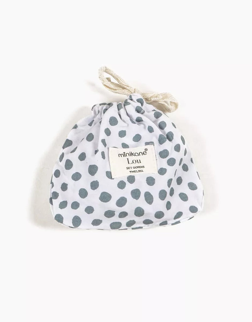 A small white drawstring pouch with blue polka dots, designed for Minikane 13" Doll Clothing—Lou Retro Romper with Headband in Cotton. The front label reads “minikane LOU, set gourde, THELMA.” Slightly gathered at the top.