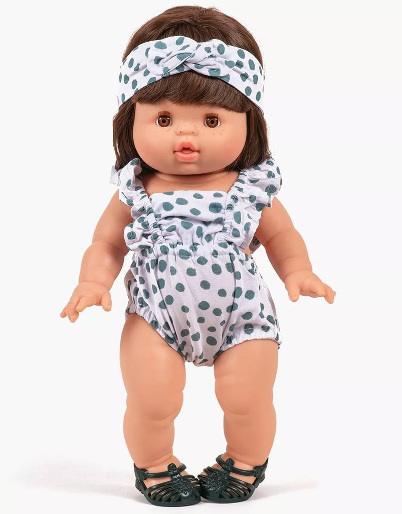 A 13" Minikane doll wears the Lou Retro Romper with Headband in cotton polka dot, paired with dark green sandals. The brown-haired doll stands facing forward against a plain white background.