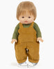 A Minikane Gordis doll with brown hair stands facing forward, dressed in an olive green jersey t-shirt and the Antoine Corduroy Overalls Set, which includes mustard yellow corduroy overalls. The doll also wears white shoes with a plaid pattern.