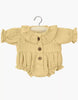 Minikane Doll Clothing | Leonore Ruffled Romper in Cotton Gauze - Vanilla: Light yellow long-sleeve romper with ruffled collar, front buttons, and gathered cuffs/legs for 34cm dolls, shown on a wooden hanger against a white background.