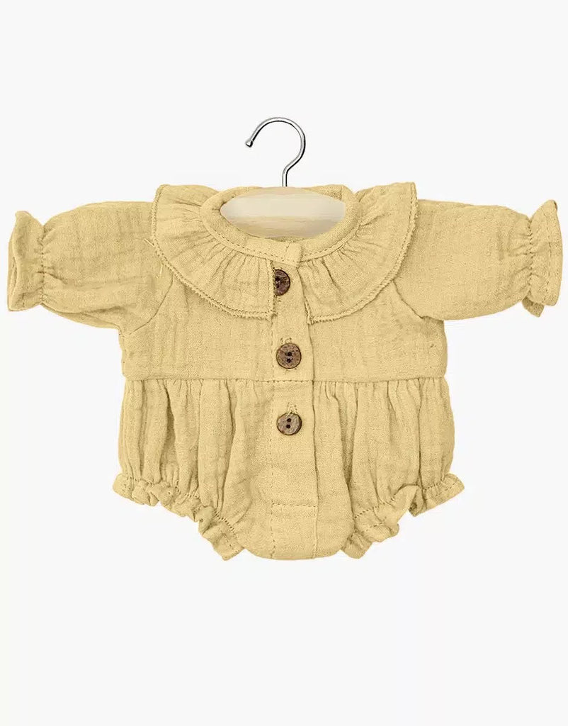 Minikane Doll Clothing | Leonore Ruffled Romper in Cotton Gauze - Vanilla: Light yellow long-sleeve romper with ruffled collar, front buttons, and gathered cuffs/legs for 34cm dolls, shown on a wooden hanger against a white background.