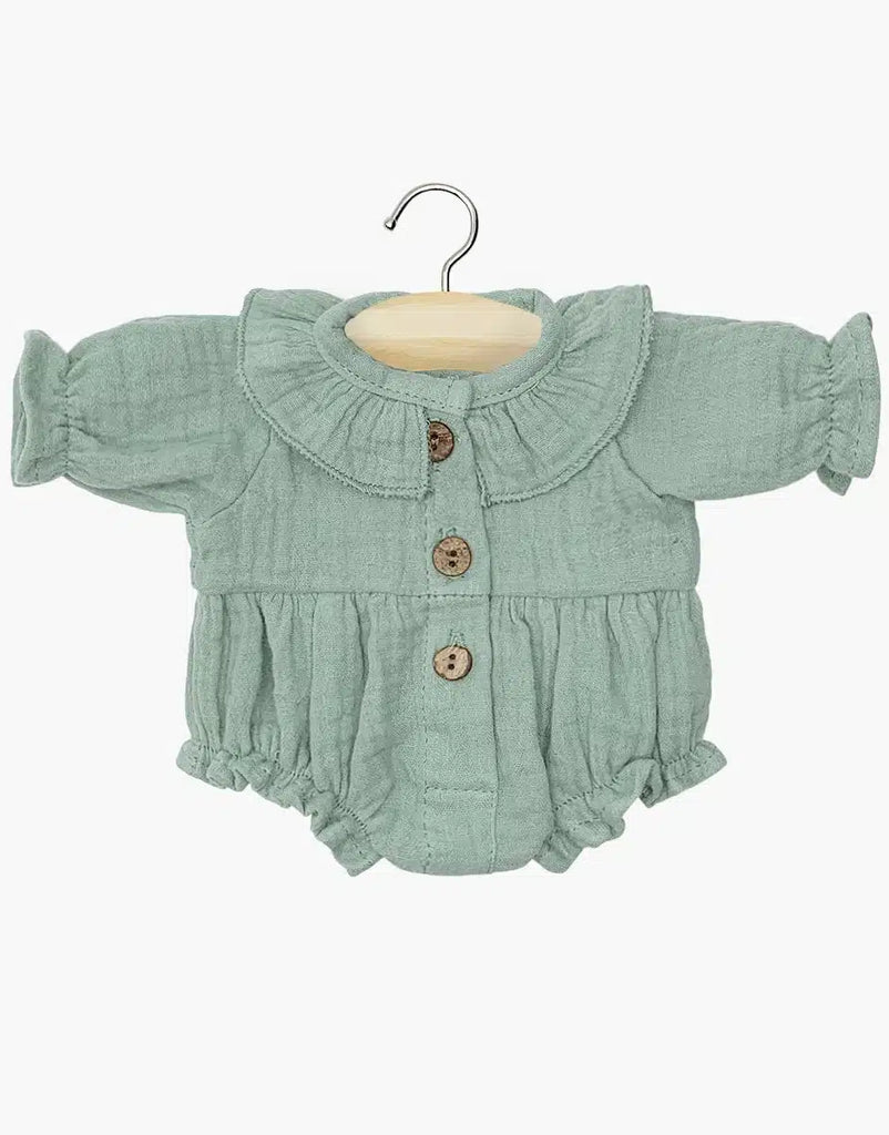 The Leonore Ruffled Jumpsuit in Baltic Green, designed for Minikane dolls, is a charming small, green cotton romper with long sleeves and three wooden buttons down the front. It is showcased on a wooden hanger. This jumpsuit features a ruffled collar and sleeves, with gathered fabric at the waist and leg openings for added style. Crafted with care in France, it is perfectly sized for your doll's wardrobe.