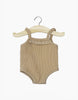 A cocoa ribbed bodysuit with spaghetti straps, perfect for Minikane Gordis dolls, hangs on a wooden hanger. The lace trim along the neckline adds charm, and it's conveniently hand washable.