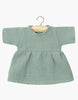 A small Faustine dress in Baltic Green for Minikane Babies hangs on a wooden hanger. This short-sleeve dress features a round neckline and slightly gathered waist for a gentle flare, enhancing its charm against the simple white background.