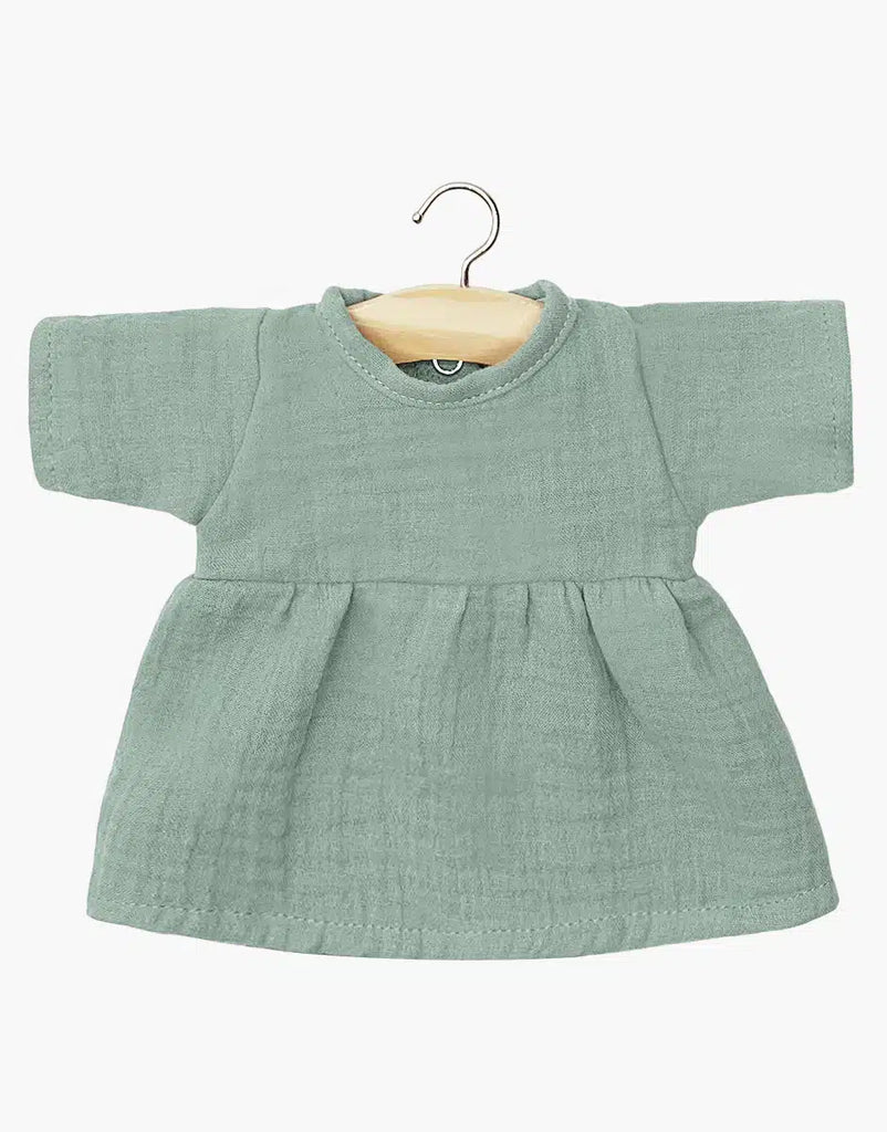 A small Faustine dress in Baltic Green for Minikane Babies hangs on a wooden hanger. This short-sleeve dress features a round neckline and slightly gathered waist for a gentle flare, enhancing its charm against the simple white background.