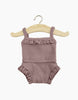 A Minikane Doll Clothing | Underwear in Dark Orchid Ribbed Knit with spaghetti straps is hanging on a wooden hanger. The romper, perfect for Minikane Gordis dolls' underwear, features delicate lace detailing on the neckline and leg openings.