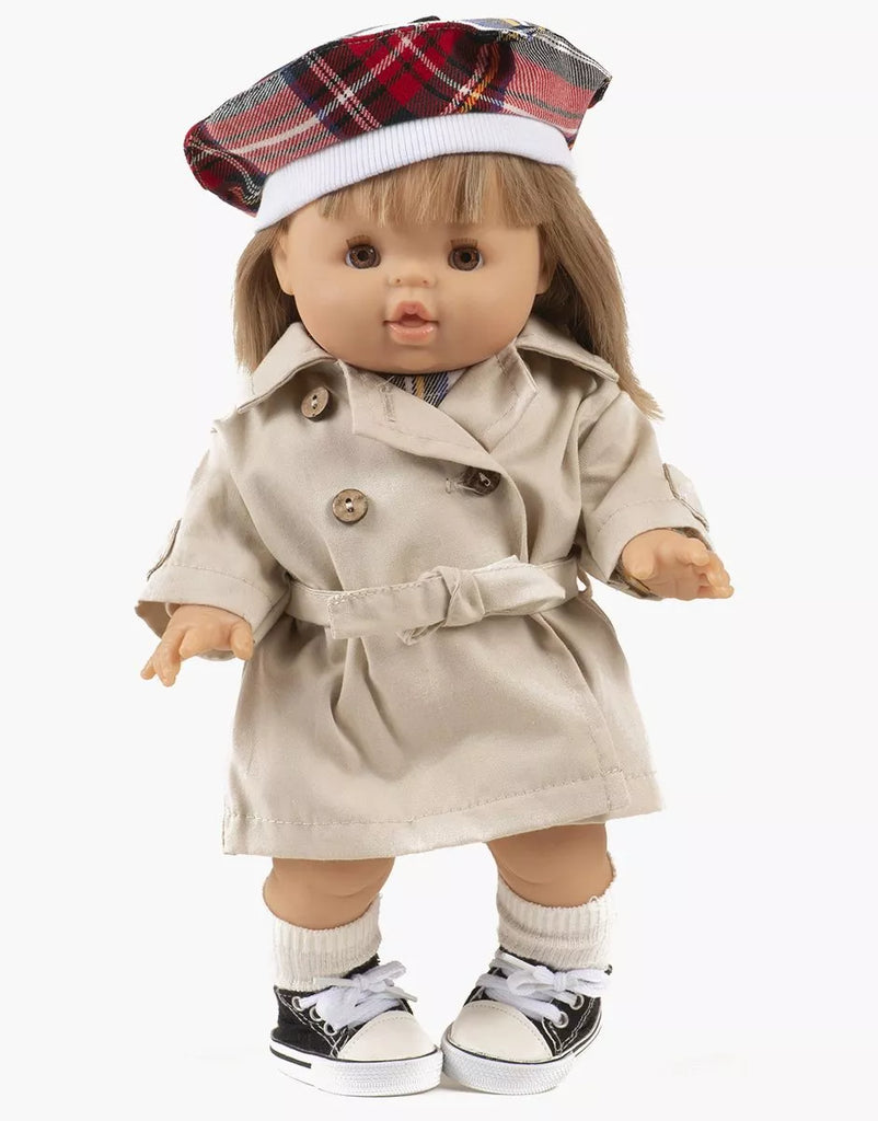 A 13-inch Minikane doll with straight blonde hair models the Tara Trench Coat in Beige Gabardine from Minikane Doll Clothing’s Back to School collection, paired with a plaid beret, white socks, and black-and-white sneakers. Made in France.