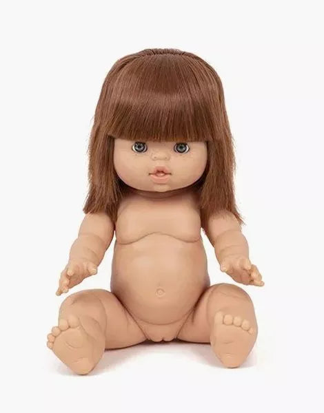 A Minikane Baby Doll With Sleeping Eyes (13") - Capucine sits upright against a white background. The anatomically correct doll has straight brown hair with bangs, blue eyes, rosy cheeks, and slightly open lips. It is unclothed, showing its detailed plastic body with arms and legs outstretched.