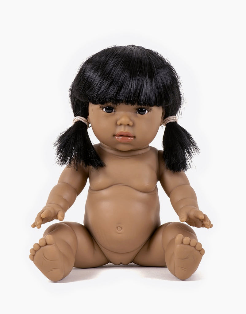 The Minikane Baby Doll (13") - Latika features a lifelike design with a medium brown skin tone, sitting upright to highlight its intricate details like fingers and toes. The doll has black hair styled in pigtails with bangs and is unclothed, anatomically correct, set against a simple white background. Clothing for the doll is sold separately.