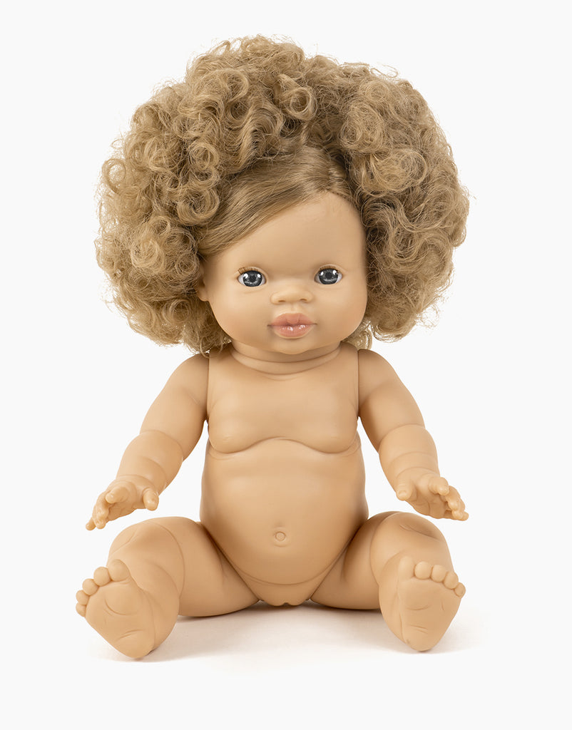 A lifelike Minikane Baby Doll (13") - Anais with curly light brown hair and blue eyes is sitting upright. The hard-bodied doll has a chubby body and detailed facial features, including a small smile. Its arms are slightly extended, and its legs are spread out in front.