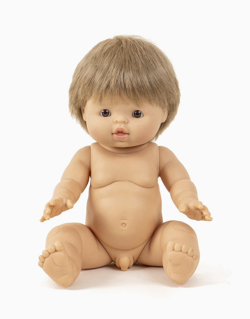 A lifelike Minikane Baby Doll (13") - Achille with light skin and short brown hair, shown sitting with legs apart and arms reaching forward. The anatomically correct doll has detailed facial features, fingers, and toes. It is unclothed against a plain white background and has a gentle natural vanilla scent.