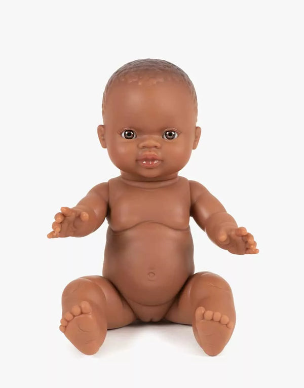 The Minikane Doll (13") - Zélie features brown skin and short hair, sitting upright with slightly spread arms and legs against a white background. This anatomically correct doll is beautifully made in Spain. Clothing sold separately.