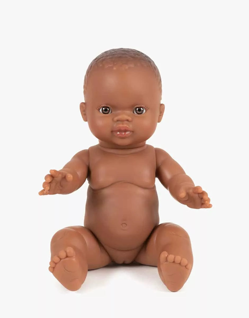 The Minikane Doll (13") - Zélie features brown skin and short hair, sitting upright with slightly spread arms and legs against a white background. This anatomically correct doll is beautifully made in Spain. Clothing sold separately.