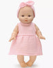 The Minikane Vintage Baby Doll (13") - Faustine with Clothing wears a pale pink textured dress and matching headband, is made from phthalate-free vinyl, and stands barefoot against a plain white background.