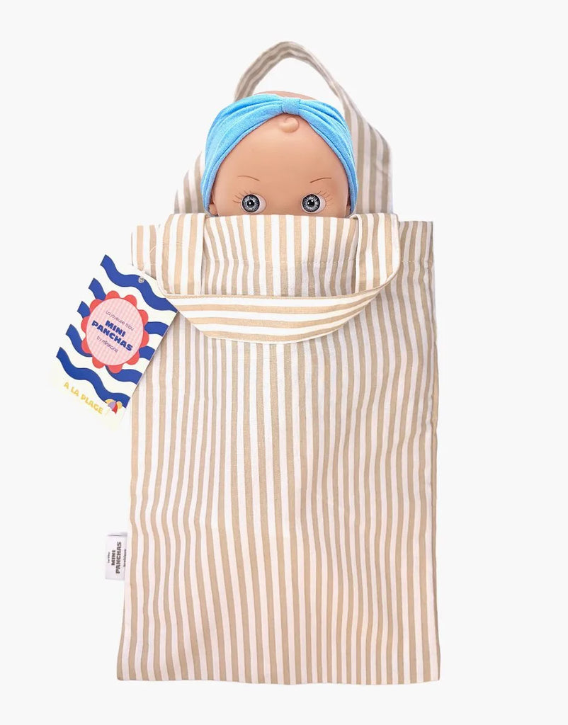 The Mini Pancha Doll - Alice with Coral Gingham Outfit peeks out of a beige and white striped fabric bag, with a colorful tag attached to the handle—perfect for imaginative play.