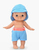 The Mini Pancha Doll - Basile with Riviera Blue Outfit features big eyes, a blue sun hat, and blue shorts with a red and white checkered waistband. Standing barefoot with arms slightly outstretched against a plain white background, this charming doll is perfect for imaginative play.