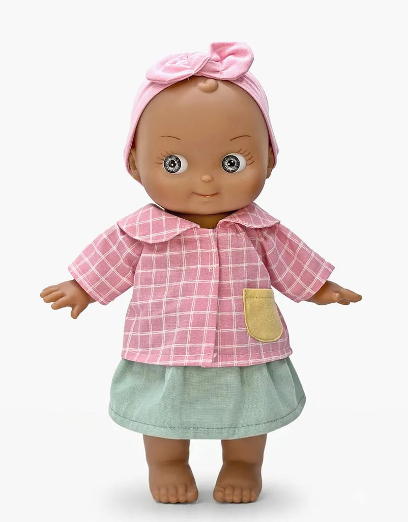 Meet the Mini Pancha Doll - Maia with Pink Checkered Outfit, featuring a charming brown complexion and wide eyes. Dressed in a pink checkered shirt, green skirt, and topped with a pink headband adorned with a bow, this high-quality vinyl doll is set against a plain white background—perfect for inspiring imaginative play.