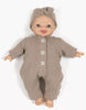A Minikane 11" Doll wears the Lili Jumpsuit & Headband in mocha cotton gauze, lying on a white background and smiling. Made in France.