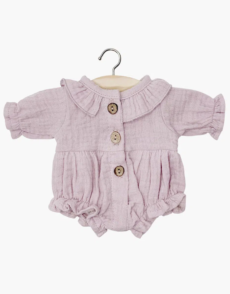 The Minikane Doll Clothing Leonore Romper in Petal Cotton Gauze showcases French design charm with its pale purple hue, long sleeves, ruffled collar, wooden buttons, elastic cuffs, and gathered waist. Hand washable and displayed on a wooden hanger, it complements your Minikane Gordis dolls perfectly.