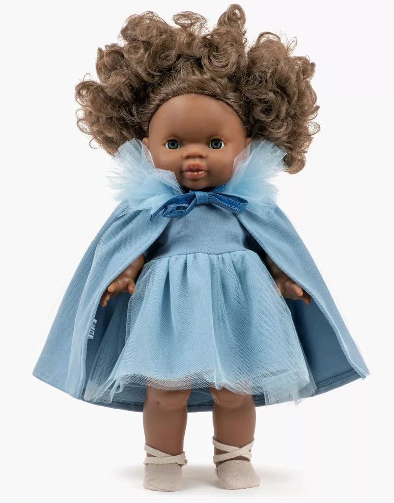 A brown-skinned 13-inch Minikane doll with curly brown hair wears the Rosana Short Sleeve Tutu in cobalt blue, with a matching tulle cape and bow, plus cream shoes. She stands against a plain white background.