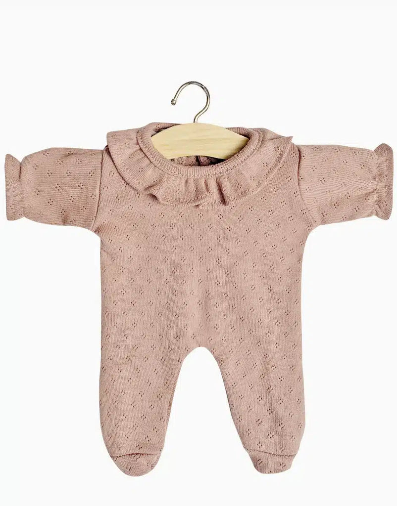 A soft pink Minikane | Camille Pajama in Orchid Pink Doll Clothing made from dotted cotton with a ruffled collar and long sleeves, displayed on a wooden hanger against a plain white background. The fabric has a delicate pattern, and the onesie includes feet covers, making it suitable for keeping Minikane Babies warm and cozy.