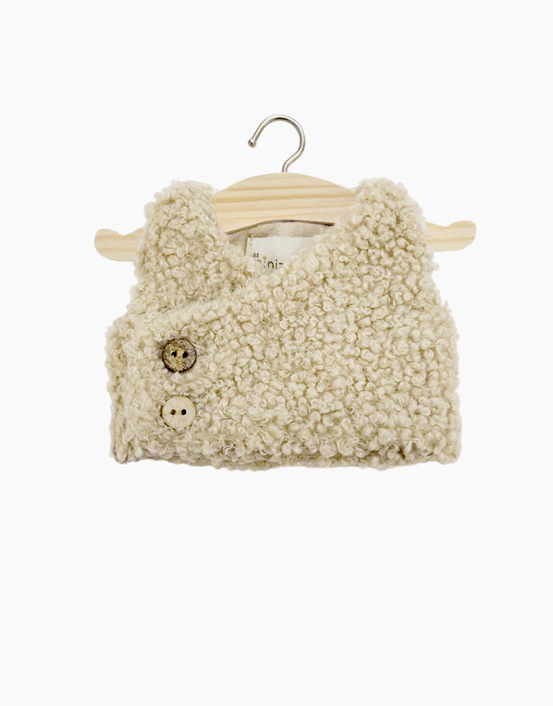 The Minikane Doll Clothing | Babies – Terry Sleeveless Vest - Beige is a textured, cream-colored, sleeveless vest with two front buttons—ideal for Minikane dolls or baby doll clothes collections. Displayed on a wooden hanger against a white background.