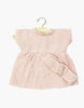 The Minikane 11" Doll Clothing | Faustine Dress & Headband in Cotton Gauze - Petal Pink features a pale pink short-sleeved dress on a wooden hanger, paired with a matching double gauze bow headband, displayed on a white background.