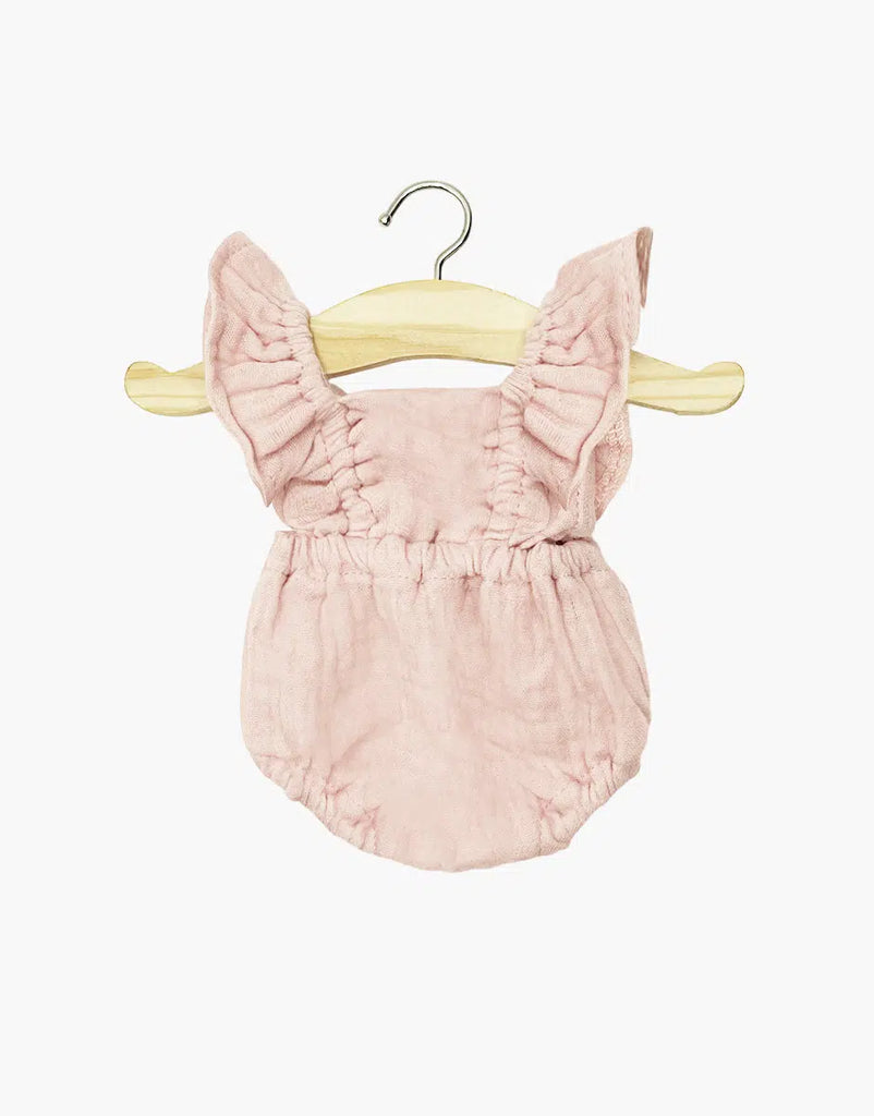 The Minikane Doll Clothing Lou Retro Romper in Cotton Gauze - Petal Pink features soft double gauze fabric and ruffled shoulder straps, designed to fit Minikane Gordis dolls. Shown on a wooden hanger against a white background.
