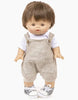 A Minikane Gordis doll with light skin, straight brown hair cut in a short bob, and brown eyes. The doll is wearing the Minikane Doll Clothing | Antonin Overalls Set Doll Clothing, which consists of linen overalls, a white t-shirt, and white sneakers with grey accents. It stands upright against a plain white background.