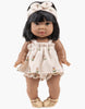 The Minikane Doll, standing in brown sandals, wears the Mila Soft Flowers Set in Terrycloth by Emile & Ida with a cream headband and short black hair, exuding French charm. Hand washable for easy care.