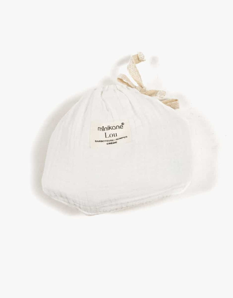 A white muslin drawstring baby bonnet with two fabric ties and an embroidered label reading "Minikane Doll Clothing | Lou Romper in Cream Cotton" is pictured against a plain white background, reminiscent of the classic Lou retro romper style designed for Minikane Gordis dolls.