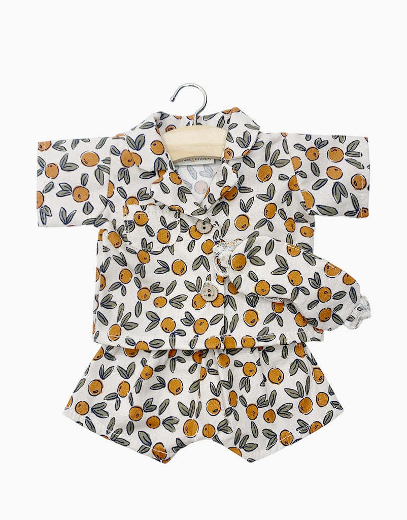 A child's two-piece clothing set on a hanger. The outfit includes a short-sleeved button-up shirt and matching shorts, both featuring a lively print of orange fruit and green leaves on a white background, perfect for pairing with Minikane Doll Clothing | Pajamas and Eye Mask in Orange Blossom.
