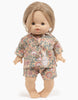 A Minikane Gordis doll with light skin, blue eyes, and shoulder-length light brown hair. The doll is wearing Minikane Doll Clothing | Laura Bohemian Bunny Pajamas featuring pink and green floral patterns and a white bunny motif on the top. Designed for 34 & 37 cm sizes, she's standing gracefully on a white background.