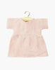 The Minikane Doll Clothing | Faustine Dress in Cotton Gauze - Petal Pink features short sleeves and soft, textured fabric. Displayed on a wooden hanger against a white background. Designed in France for Minikane Gordis dolls.