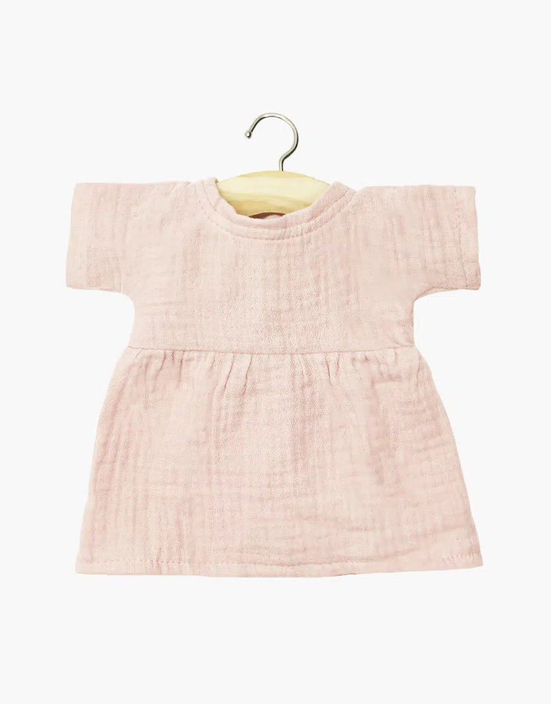 The Minikane Doll Clothing | Faustine Dress in Cotton Gauze - Petal Pink features short sleeves and soft, textured fabric. Displayed on a wooden hanger against a white background. Designed in France for Minikane Gordis dolls.