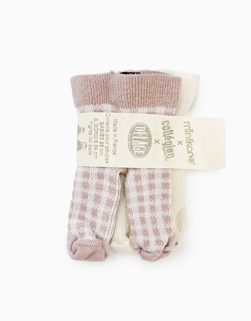 A pack of Minikane Doll Clothing | Pack of Two Leggings in Ecru and Pink Checkers with the label "rik&rok x Col&Kimi." The leggings, all hand washable, feature different designs: a pair with pink and white checkered patterns and a cream-colored pair. The leggings are held together by a beige paper band.