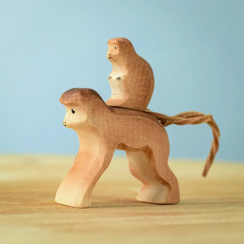 The Bumbu Wooden Monkey Set is a small handcrafted sculpture showcasing two monkeys, one joyfully riding on the back of the other. With its minimalist design and smooth curves in light brown hues, this eco-friendly toy is perfect for any collection. The soft pastel blue background enhances its enchanting appeal.