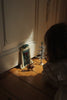 A child looks at a Konges Sloejd Christmas Door, a small decorated tree, and a toy cat placed on a wooden floor.