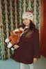 A smiling girl wearing a beanie and coat holds a cuddly Konges Sloejd Fiona Horse toy.