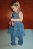 A toddler in a denim dress and pants with sparkly polka dots holds a pink, circular Konges Sloejd Tut Kitty Shoulder Bag.