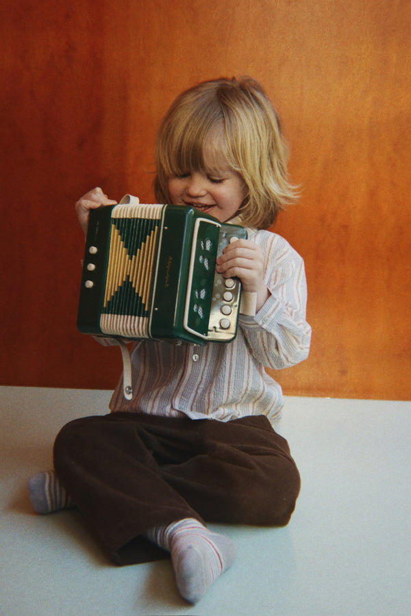 A young child sits on the floor playing a small green 10-key Konges Sloejd Accordian.