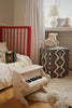 A Konges Sloejd Accordian 10-key button toy resting on a child’s bed next to a small wooden piano.