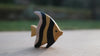 The Handmade Holzwald Moorish Idol Fish is a small wooden toy with yellow and black stripes, standing upright on a light surface—perfect for imaginative, educational play.