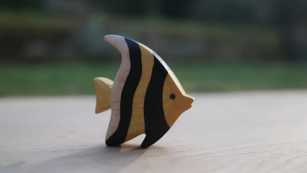 The Handmade Holzwald Moorish Idol Fish is a small wooden toy with yellow and black stripes, standing upright on a light surface—perfect for imaginative, educational play.