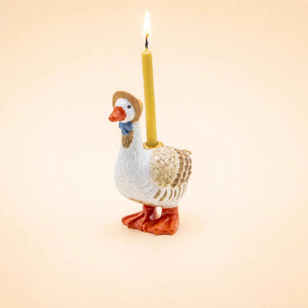 A ceramic “Mother Goose Cake Topper” figurine wearing a small hat holds a lit yellow candle on its back, set against a plain beige background—perfect as a handcrafted birthday decoration or charming collectible keepsake.