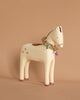 The Maileg Wooden Horse Candle Holder - Large features a delightful cream-colored design with painted pink hooves and star patterns, standing on a beige surface to create a cozy Christmas ambiance. It is beautifully adorned with a gold tinsel garland and colorful bells around its neck.